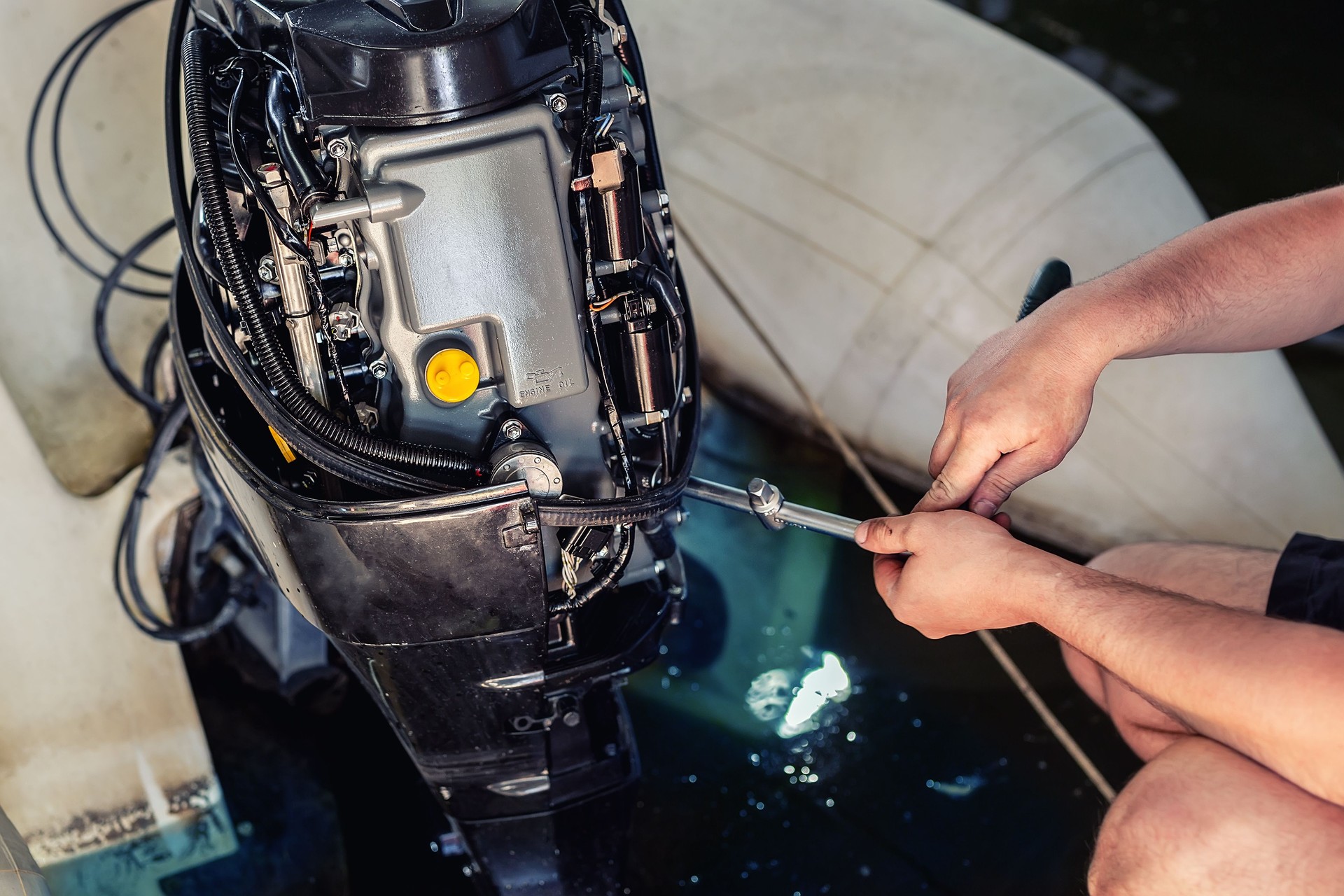 mechanic repairing inflatable motorboat engine at boat garage. Ship engine seasonal service and maintenance. Vessel motor with open cover